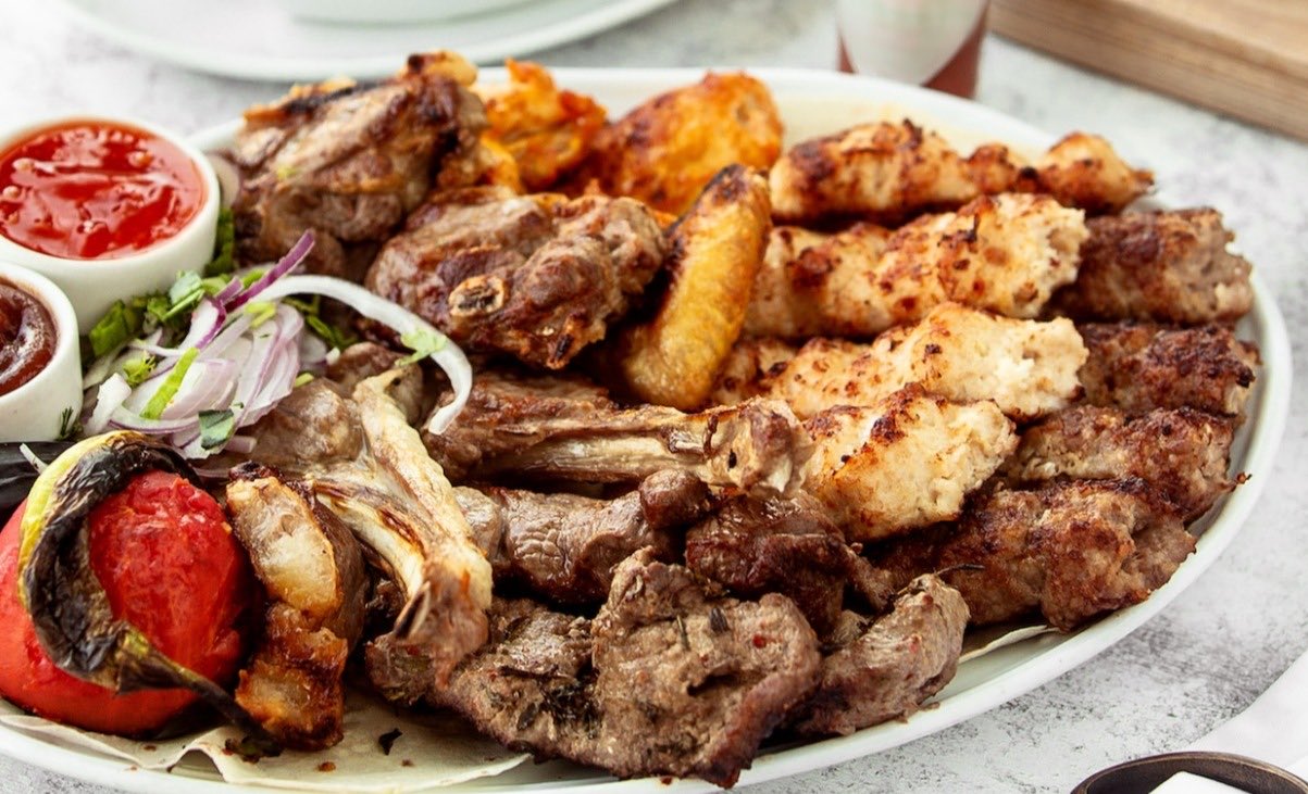 A family sharing platter of grilled meats, chicken wings and lamb ribs